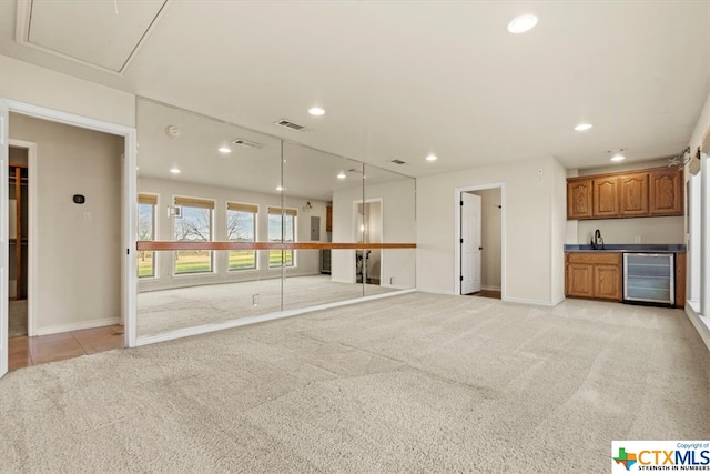 unfurnished living room featuring light colored carpet, beverage cooler, and indoor bar