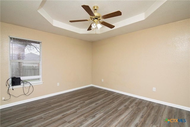 empty room featuring dark hardwood / wood-style flooring, a tray ceiling, and ceiling fan