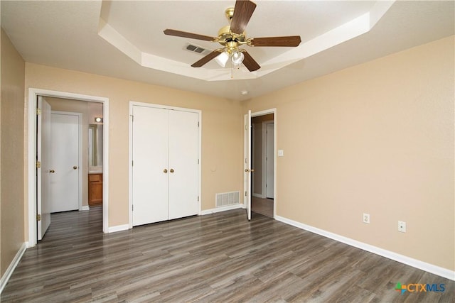 unfurnished bedroom with a raised ceiling, dark hardwood / wood-style floors, ceiling fan, and a closet