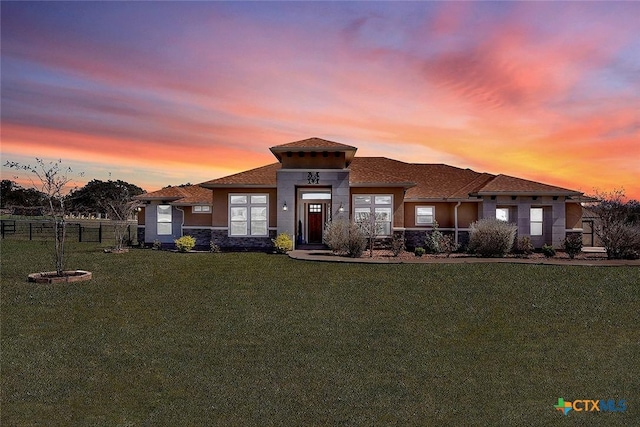 prairie-style home featuring stucco siding, a lawn, and fence