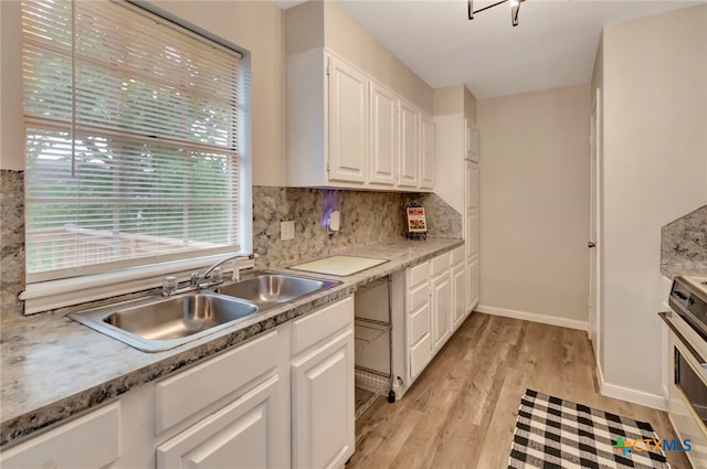 kitchen featuring tasteful backsplash, sink, light hardwood / wood-style flooring, stainless steel stove, and white cabinetry