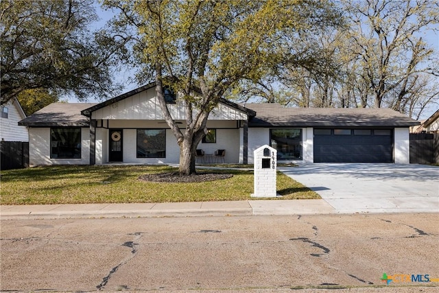 view of front of property with concrete driveway, a front lawn, an attached garage, and fence