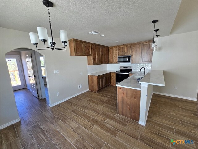 kitchen with dark hardwood / wood-style flooring, kitchen peninsula, hanging light fixtures, sink, and appliances with stainless steel finishes