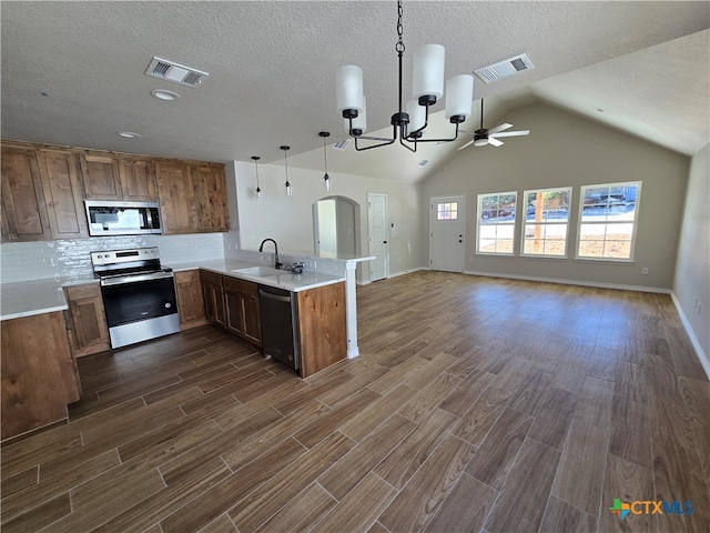 kitchen featuring kitchen peninsula, dark wood-type flooring, appliances with stainless steel finishes, and decorative light fixtures