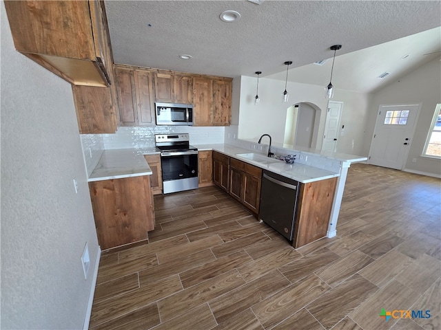 kitchen with vaulted ceiling, kitchen peninsula, hanging light fixtures, sink, and appliances with stainless steel finishes