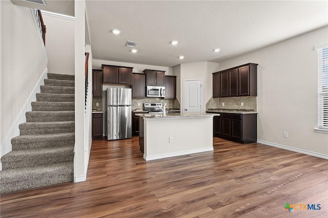 5101 Hacienda Dr, Killeen, TX 76549 - kitchen featuring appliances with stainless steel finishes, dark brown cabinets, backsplash, a kitchen island with sink, and recessed lighting