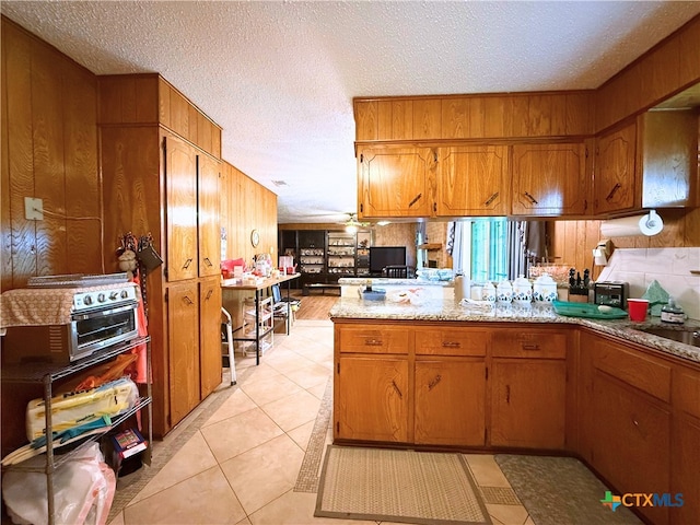 1901 Muir Dr, Killeen, TX 76543 - kitchen featuring brown cabinets, a peninsula, a textured ceiling, light tile patterned floors, and wooden walls
