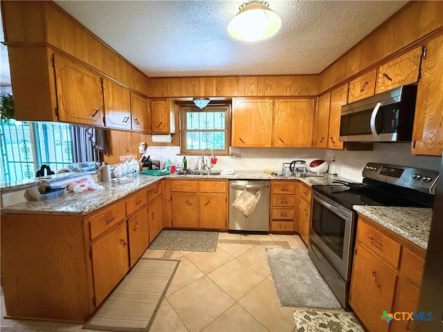 1901 Muir Dr, Killeen, TX 76543 - kitchen featuring stainless steel appliances, a peninsula, a textured ceiling, brown cabinets, and light stone counters