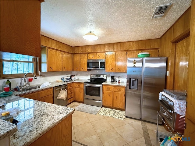 1901 Muir Dr, Killeen, TX 76543 - kitchen featuring appliances with stainless steel finishes, brown cabinets, a textured ceiling, wood walls, and light tile patterned floors