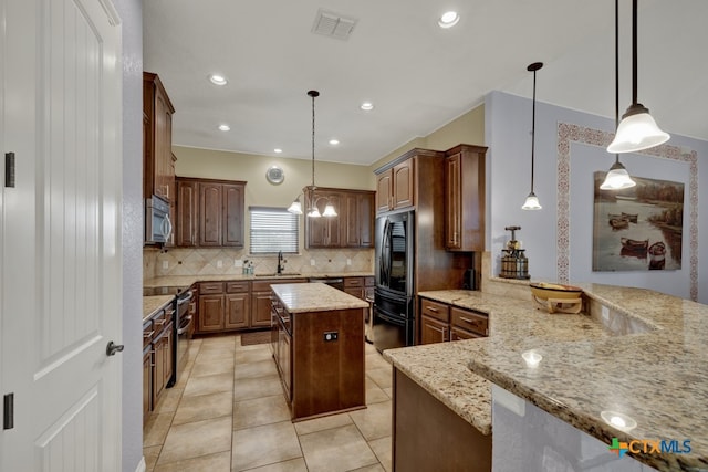 kitchen with kitchen peninsula, light stone counters, stainless steel appliances, a kitchen island, and hanging light fixtures