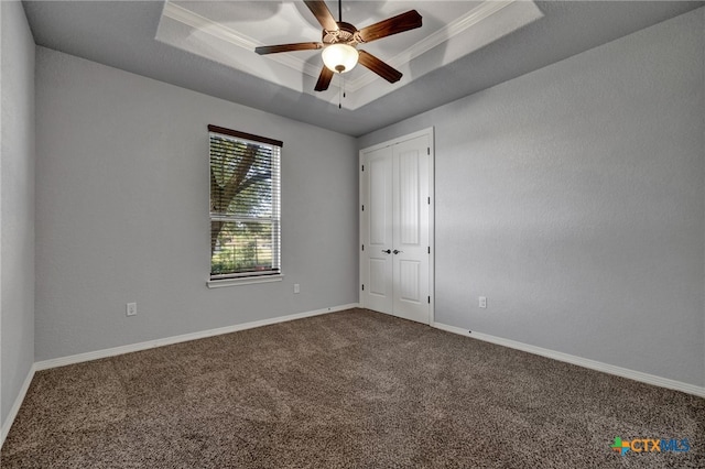 empty room with a raised ceiling, ceiling fan, carpet, and ornamental molding