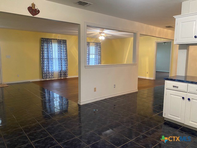 unfurnished living room with baseboards, visible vents, a ceiling fan, and dark tile patterned flooring