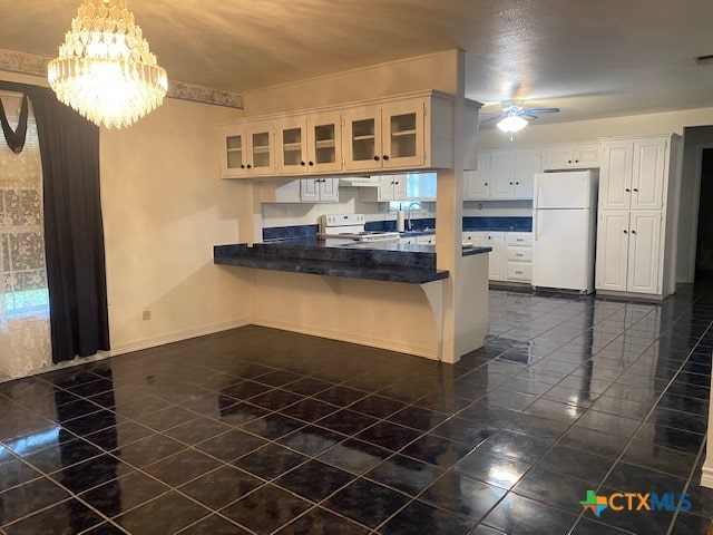 kitchen with ceiling fan with notable chandelier, a peninsula, white appliances, a kitchen bar, and glass insert cabinets