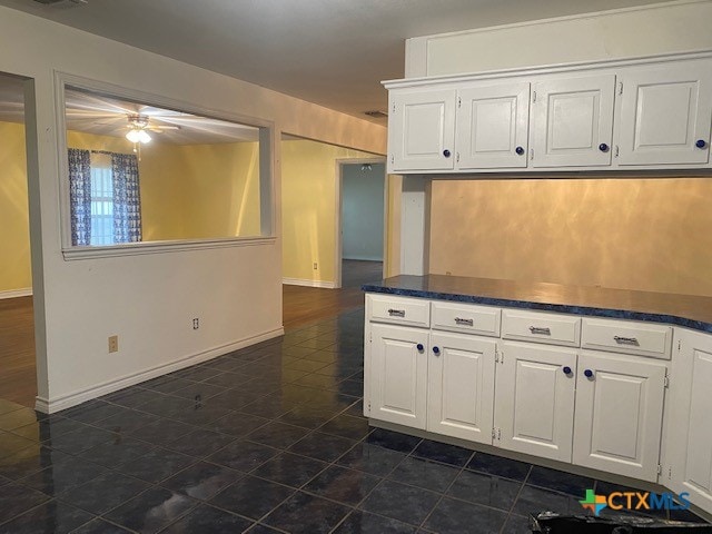 kitchen featuring dark countertops, ceiling fan, baseboards, and white cabinets