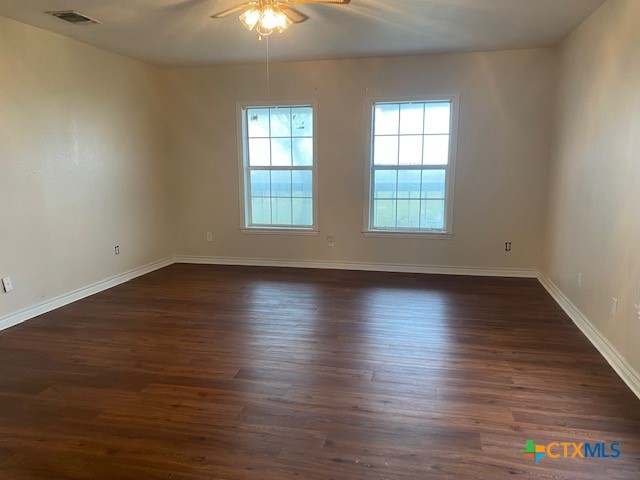 unfurnished room with dark wood-type flooring, visible vents, and baseboards