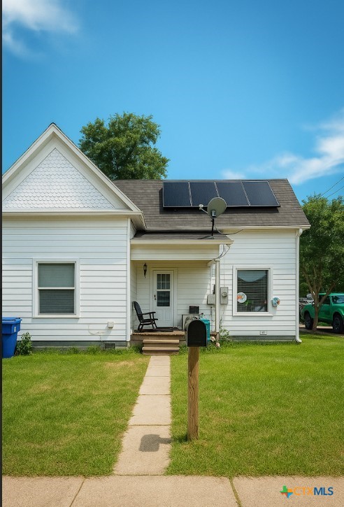 202 Clark St, Yoakum, TX 77995 - view of front facade featuring roof mounted solar panels, a front lawn, and roof with shingles