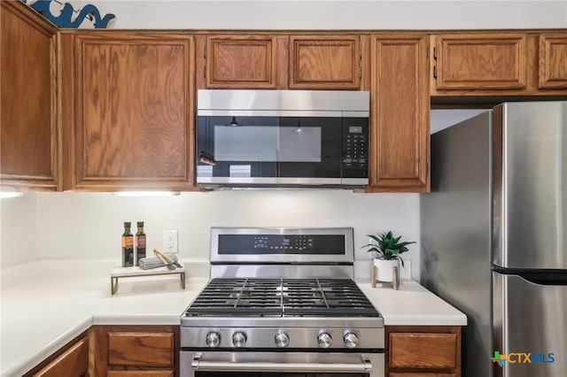 kitchen featuring stainless steel appliances, brown cabinetry, and light countertops