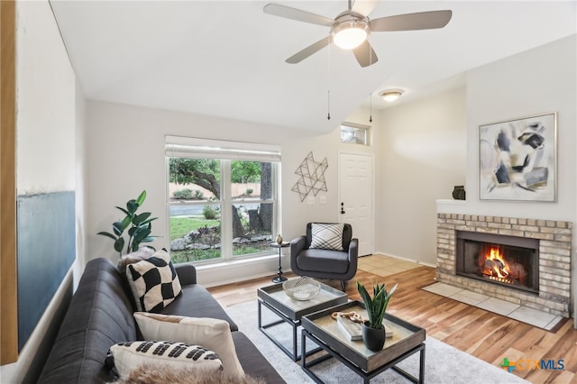 living area featuring vaulted ceiling, ceiling fan, a brick fireplace, and wood finished floors