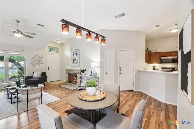 dining space featuring light wood finished floors, ceiling fan, a fireplace, and baseboards