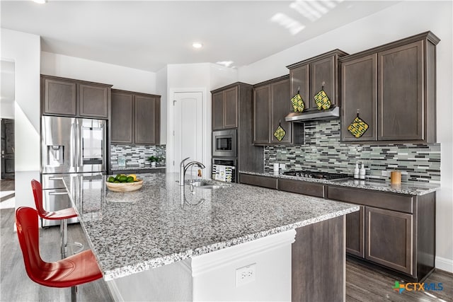 kitchen with light stone counters, stainless steel appliances, dark hardwood / wood-style floors, sink, and a breakfast bar area