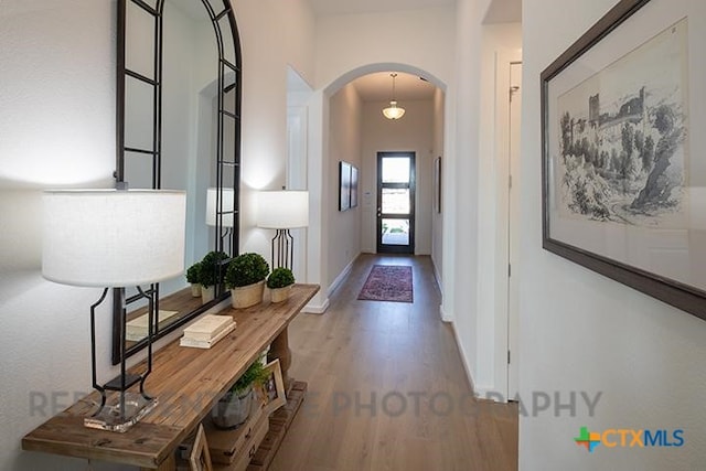 interior space with baseboards, arched walkways, and wood finished floors