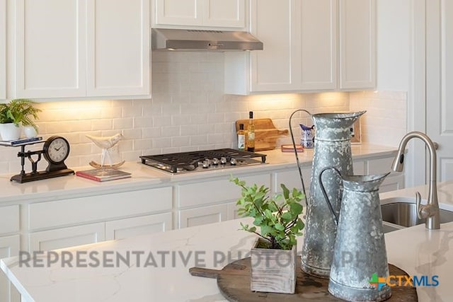 kitchen with white cabinets, stainless steel gas cooktop, under cabinet range hood, and tasteful backsplash