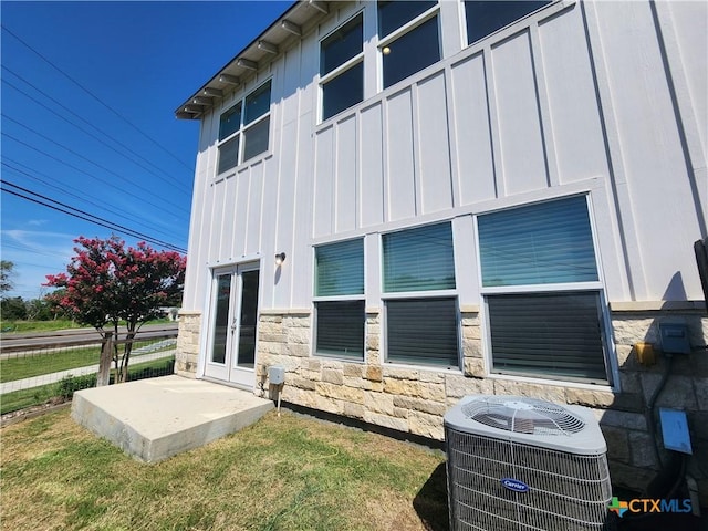 exterior space with cooling unit, french doors, board and batten siding, and stone siding