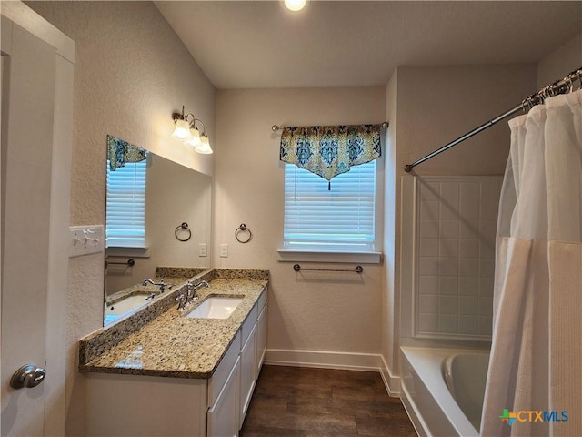 full bath featuring wood finished floors, shower / tub combo, baseboards, vanity, and a textured wall