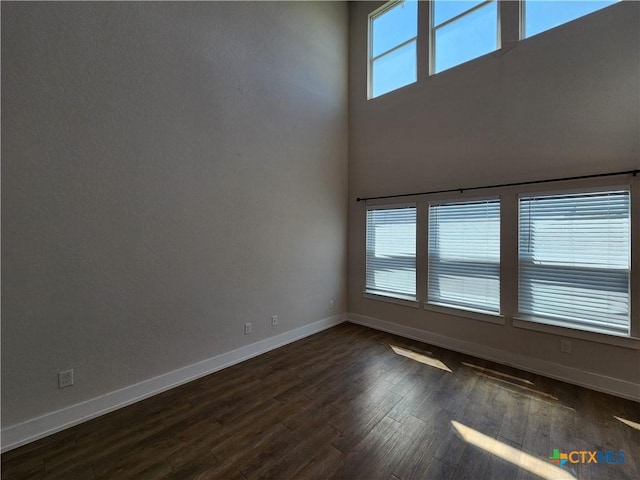 empty room with dark wood finished floors, plenty of natural light, baseboards, and a towering ceiling