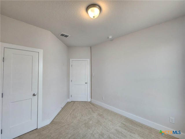 empty room with a textured ceiling, baseboards, visible vents, and light carpet