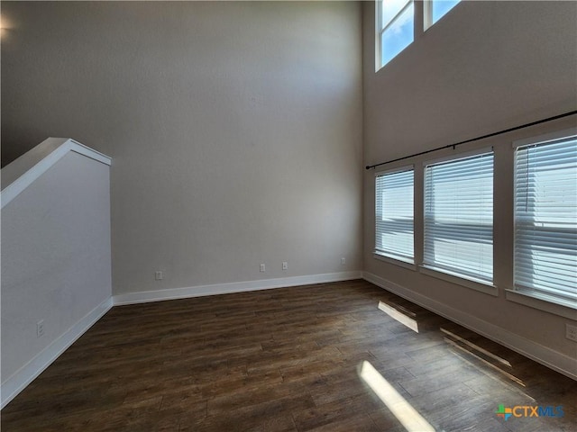 unfurnished room featuring dark wood-style floors, baseboards, and a towering ceiling