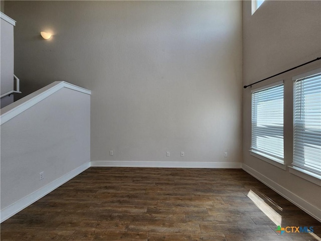 spare room featuring dark wood finished floors, baseboards, and a towering ceiling