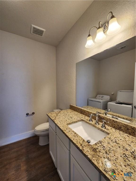 bathroom featuring wood finished floors, baseboards, visible vents, toilet, and washer and clothes dryer