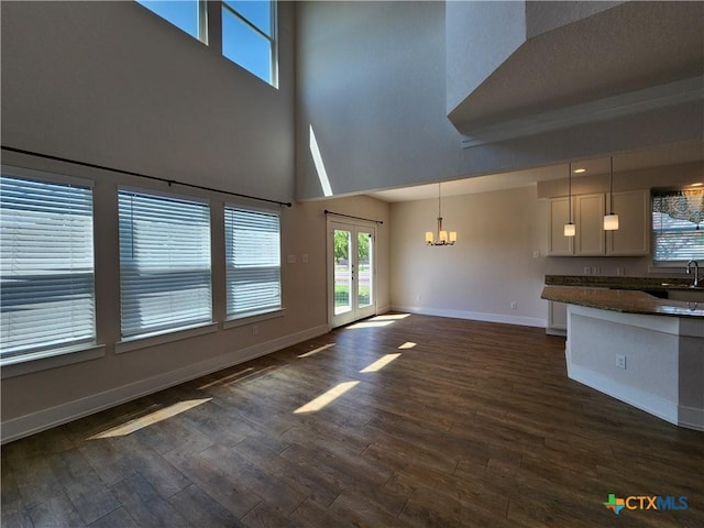 unfurnished living room featuring a notable chandelier, a sink, dark wood-style floors, french doors, and baseboards