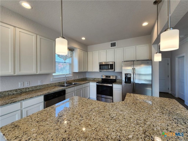 kitchen with visible vents, light stone counters, stainless steel appliances, white cabinetry, and a sink