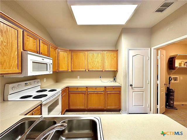 kitchen featuring white appliances, sink, vaulted ceiling, and light tile patterned flooring