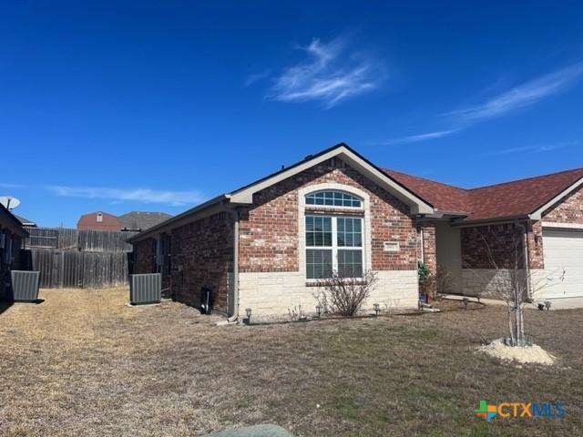 view of side of home featuring a garage, brick siding, and central air condition unit