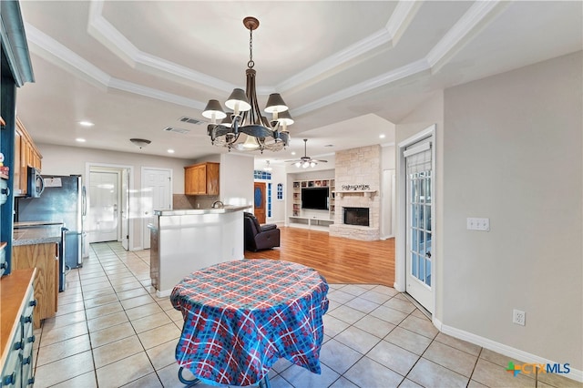 kitchen with a tray ceiling, a fireplace, light tile patterned floors, ceiling fan with notable chandelier, and ornamental molding