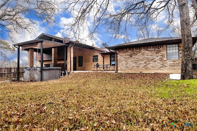 rear view of property featuring a yard, brick siding, and a hot tub