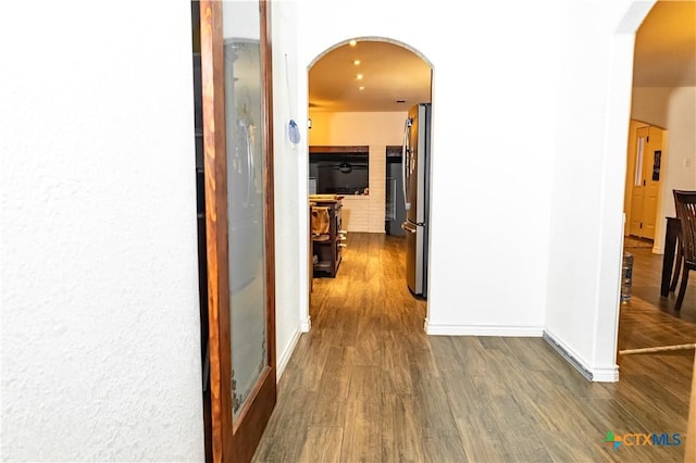 hall with baseboards, arched walkways, and dark wood-type flooring