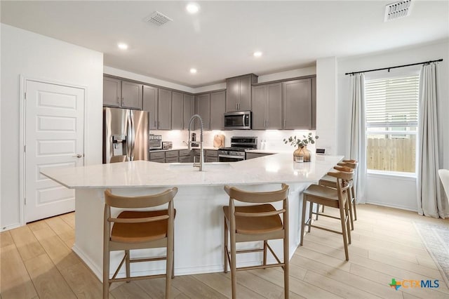 4648 Padula Dr, Round Rock, TX 78665 - kitchen with appliances with stainless steel finishes, light wood finished floors, a kitchen breakfast bar, gray cabinets, and a peninsula