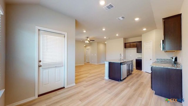 kitchen with an island with sink, sink, stainless steel appliances, light stone countertops, and light hardwood / wood-style flooring