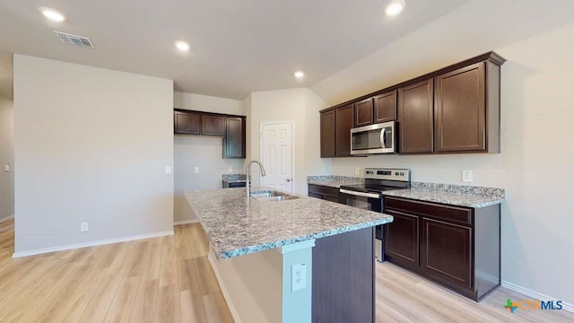 kitchen with sink, light stone counters, appliances with stainless steel finishes, a kitchen island with sink, and light hardwood / wood-style floors