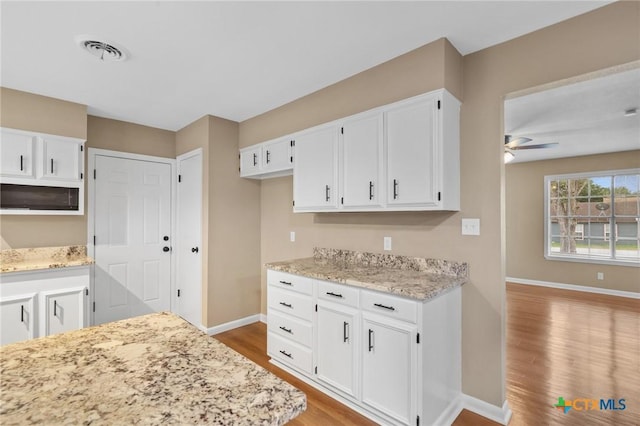 454 W Ward St, Goliad, TX 77963 - kitchen featuring wood finished floors, white cabinetry, a ceiling fan, white microwave, and light stone counters