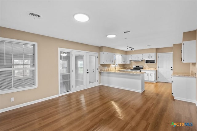 454 W Ward St, Goliad, TX 77963 - kitchen with electric range, a peninsula, wood finished floors, white cabinets, and under cabinet range hood