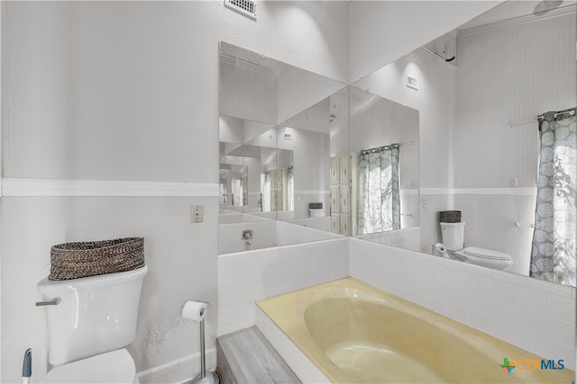 bathroom with tiled bath, toilet, and ornamental molding