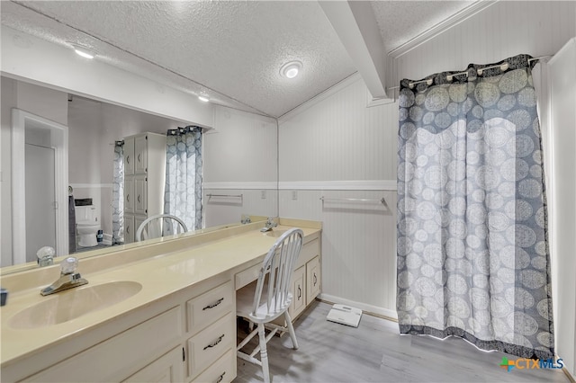 bathroom featuring wood-type flooring, crown molding, vanity, a textured ceiling, and toilet