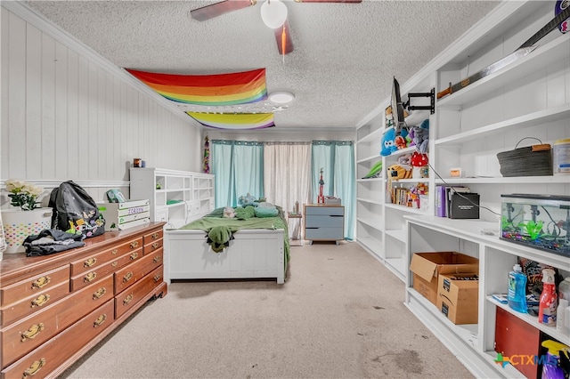 carpeted bedroom with a textured ceiling, wood walls, ceiling fan, and crown molding