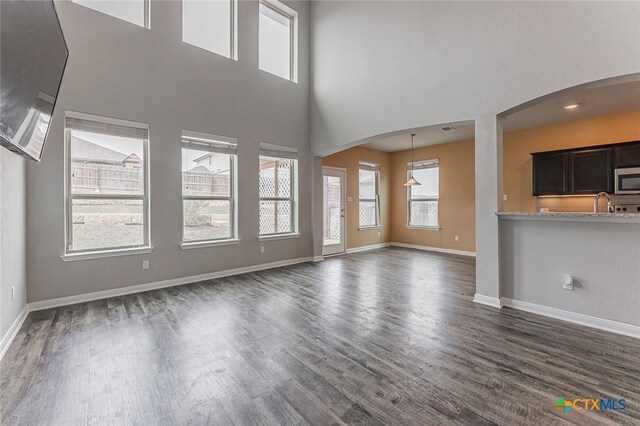 1233 Jester Ct, Copperas Cove, TX 76522 - unfurnished living room featuring baseboards, arched walkways, a towering ceiling, and dark wood-type flooring