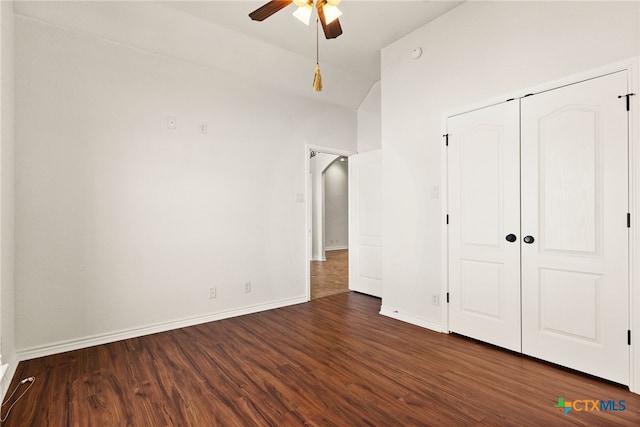 unfurnished bedroom featuring a closet, baseboards, lofted ceiling, and dark wood-style flooring